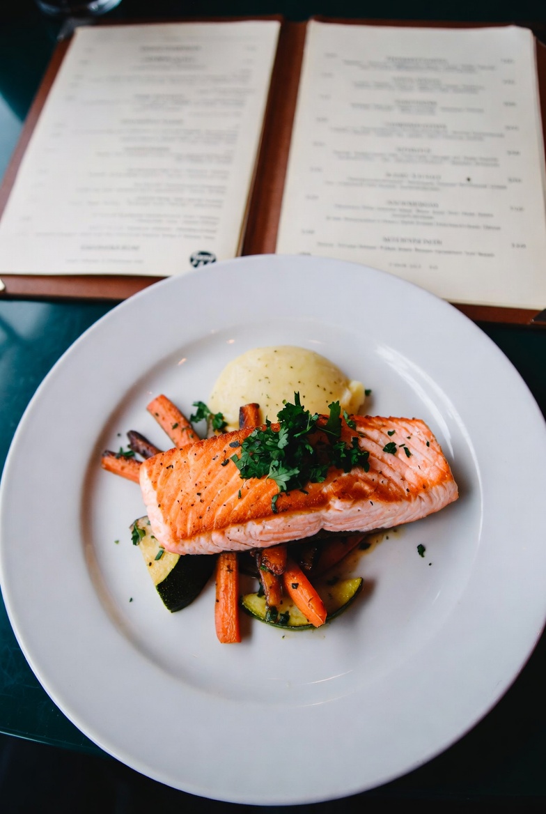 A plated salmon dish photographed next to the restaurant's open menu — the Dish & Menu scan mode